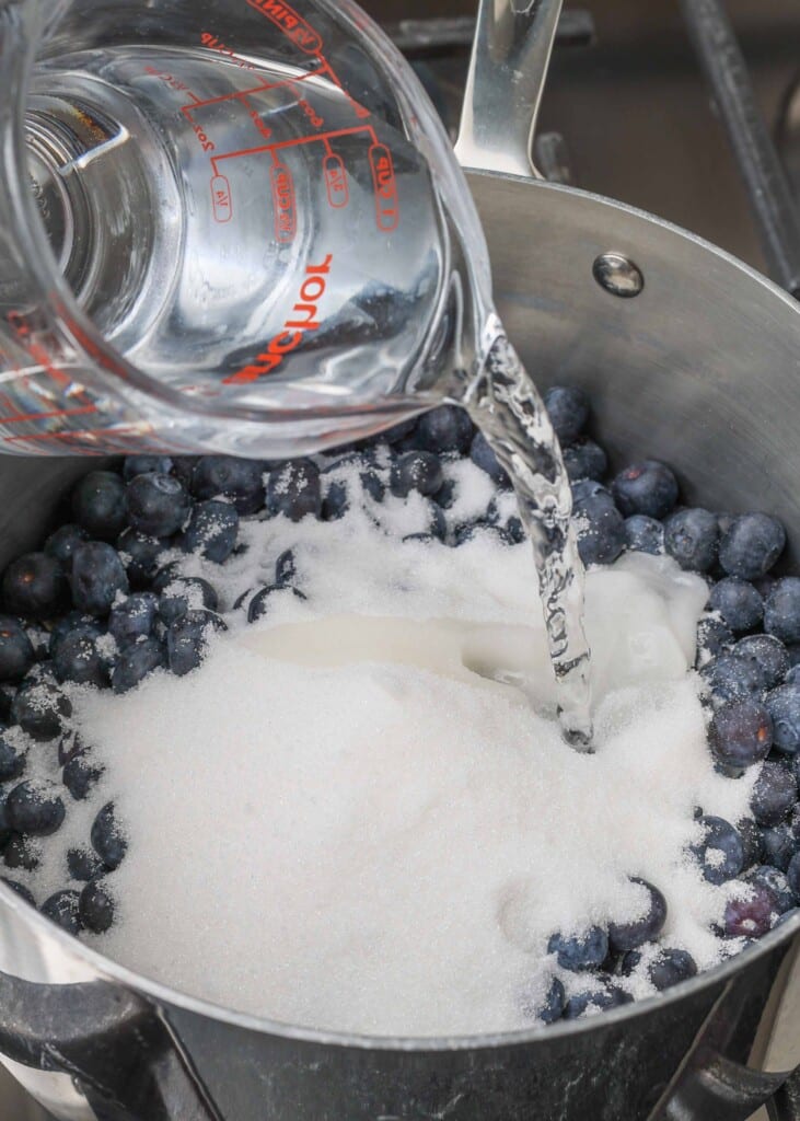 an action shot of water being poured over the sugar and blueberries in a pot