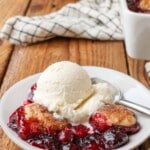 cobbler made with cherries on small white plate on wooden table