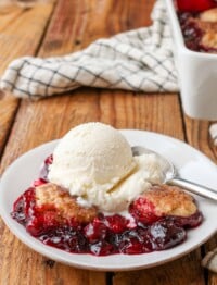 cobbler made with cherries on small white plate on wooden table