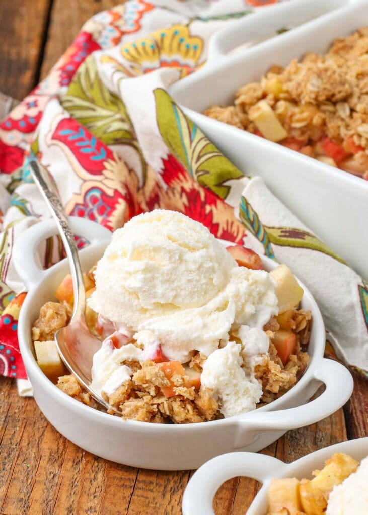 close up of apple crisp with rhubarb with ice cream on top and spoon in bowl