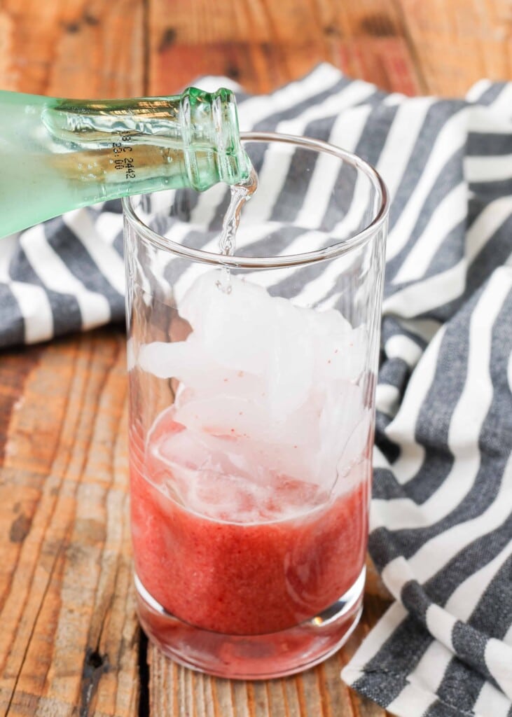 tall glass of cherry flavored lemonade on wooden table, water poured into cherry mixture