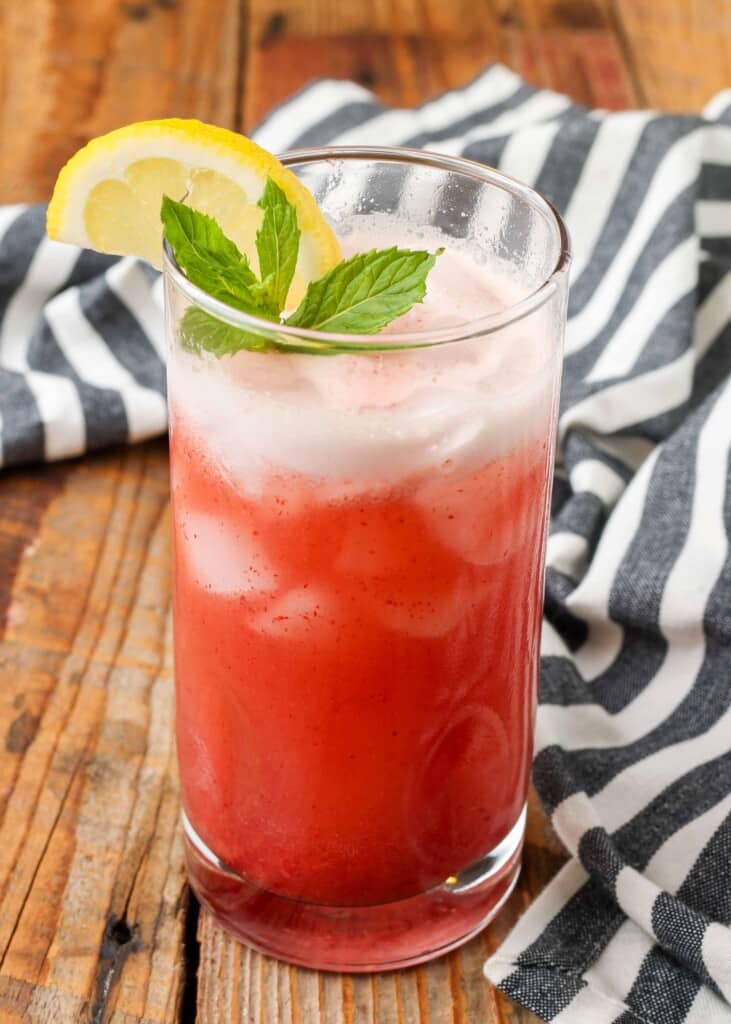 tall glass of cherry flavored lemonade with lemon wedge and mint 