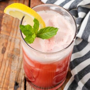 tall glass of cherry flavored lemonade with lemon wedge and mint