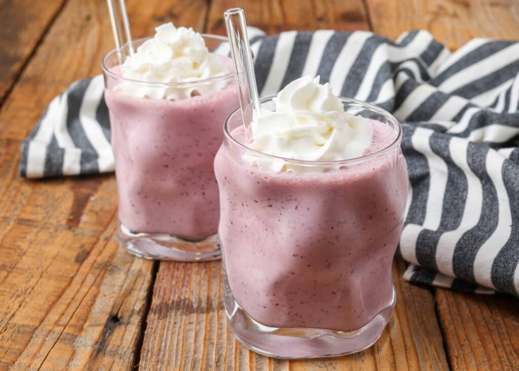 glasses holding pinnk milkshakes with glass straws on wooden table