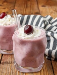 cherry milkshakes in glasses with glass straws topped with cherries and whipped cream