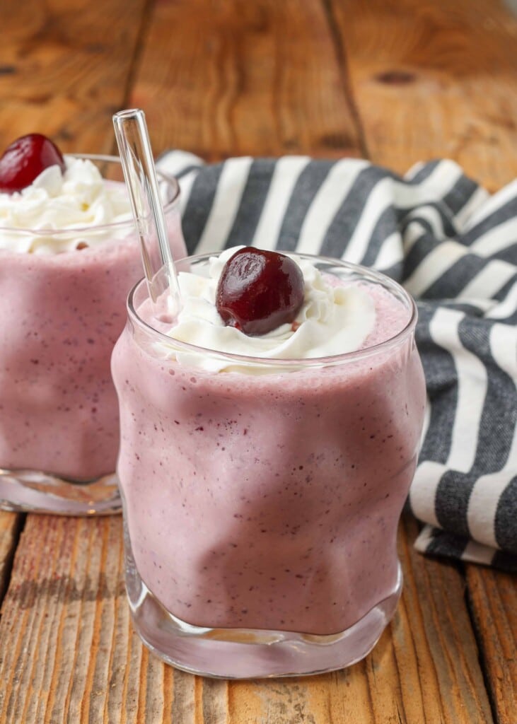 cherry milkshakes in glasses with glass straws topped with cherries and whipped cream