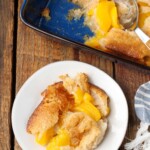 serving of peach cobbler on plate next to baking dish