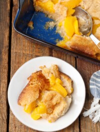 serving of peach cobbler on plate next to baking dish