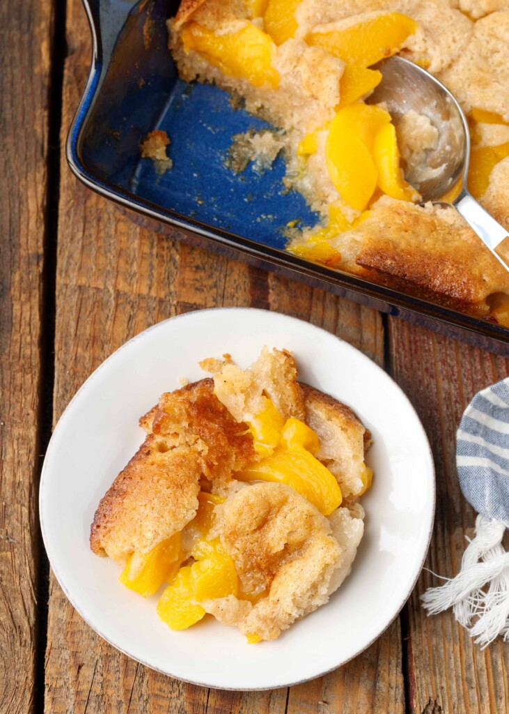 serving of peach cobbler on plate next to baking dish