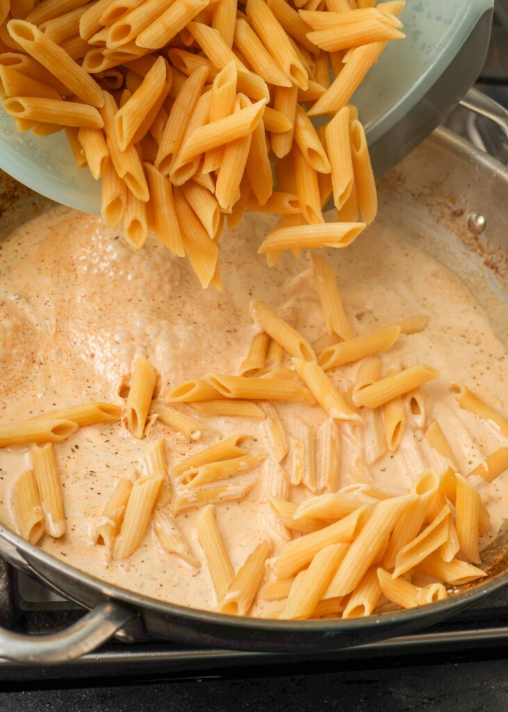 Pouring cooked pasta into creamy sauce