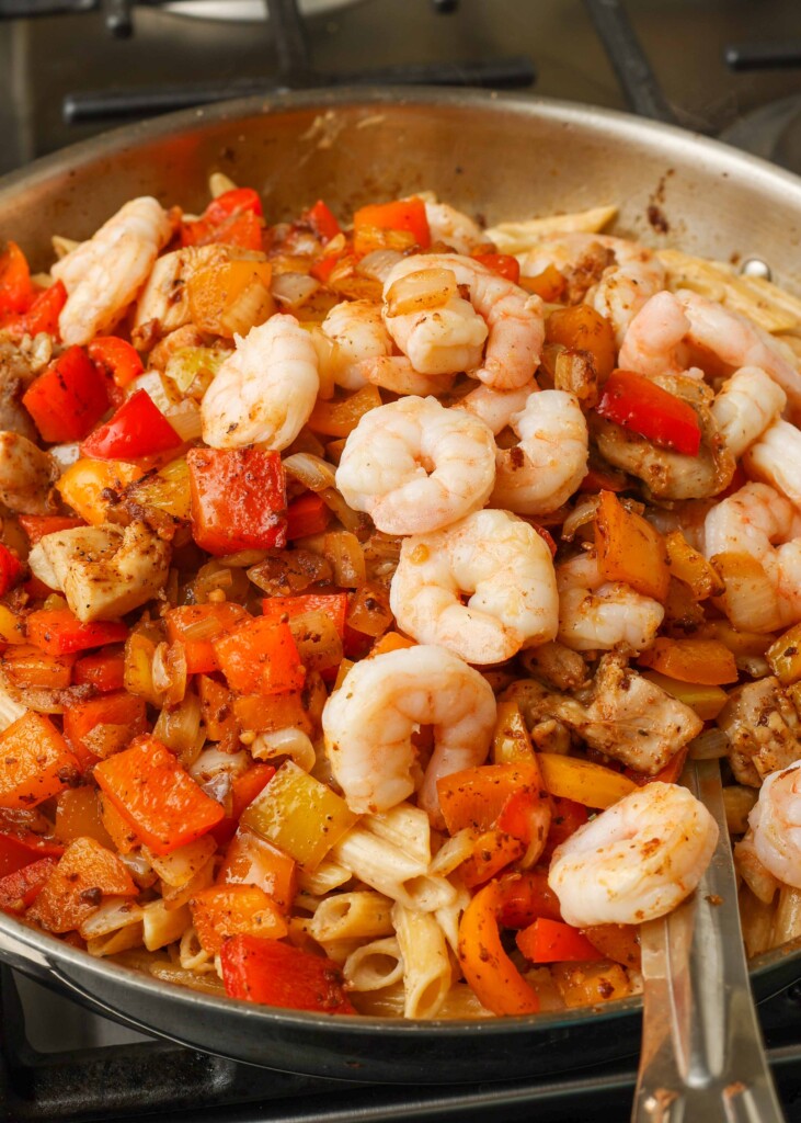 Close-up shot on chicken, shrimp, pasta, and bell peppers in a stovetop pan