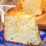 pineapple angel food cake on a cutting board with a slice on a blue plate on a wooden table