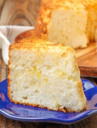 pineapple angel food cake on a cutting board with a slice on a blue plate on a wooden table