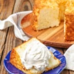 pineapple angel food cake on a cutting board with a whipped cream topped slice on a blue plate on a wooden table