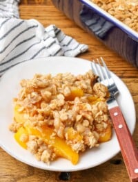 small white plate holding peach crisp with wooden fork