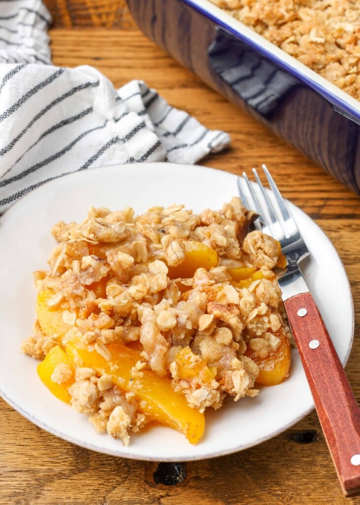 small white plate holding peach crisp with wooden fork