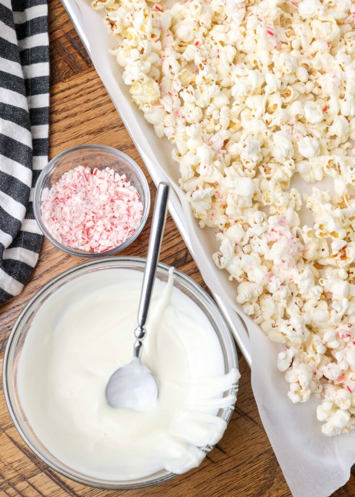 popcorn on tray next to melted white chocolate and crushed candy canes