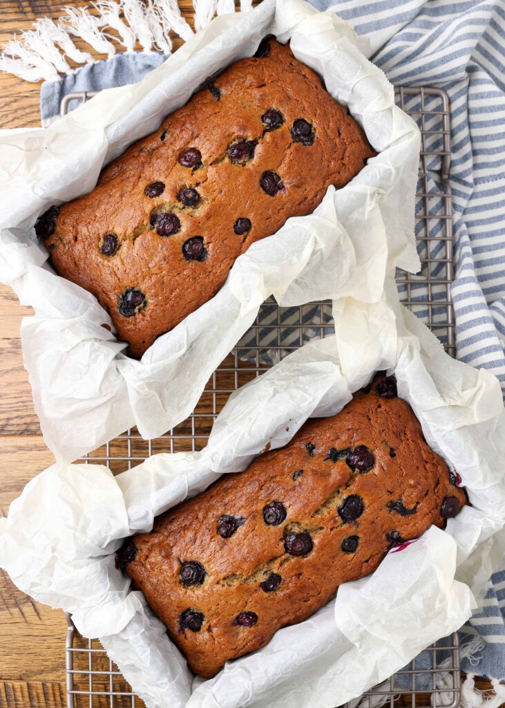 two loaves of blueberry banana bread on a cutting board with a tea towel