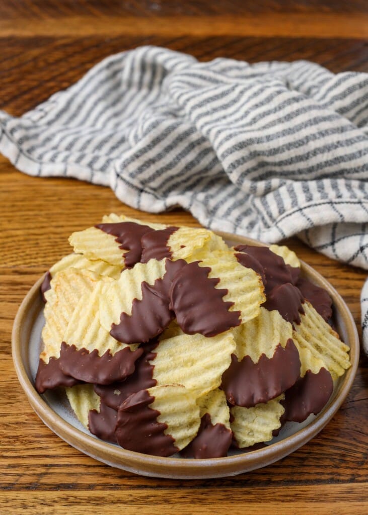 chocolate dipped potato chips on a plate with a striped towel in the background