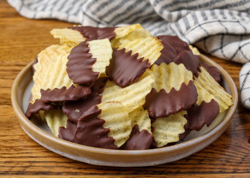 chocolate dipped potato chips on a plate with a striped towel in the background