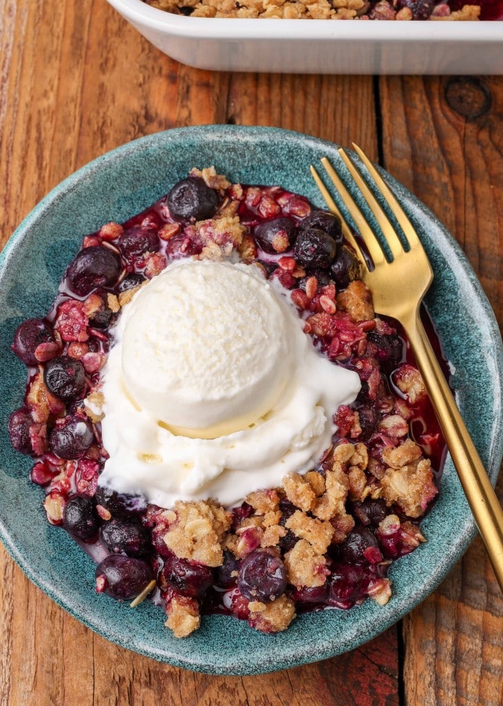 Blueberry Crisp with vanilla ice cream on blue plate with gold fork