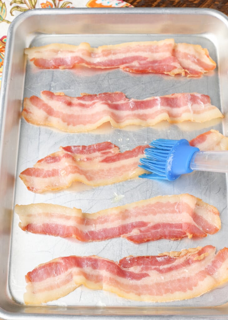brushing butter over bacon on sheet pan