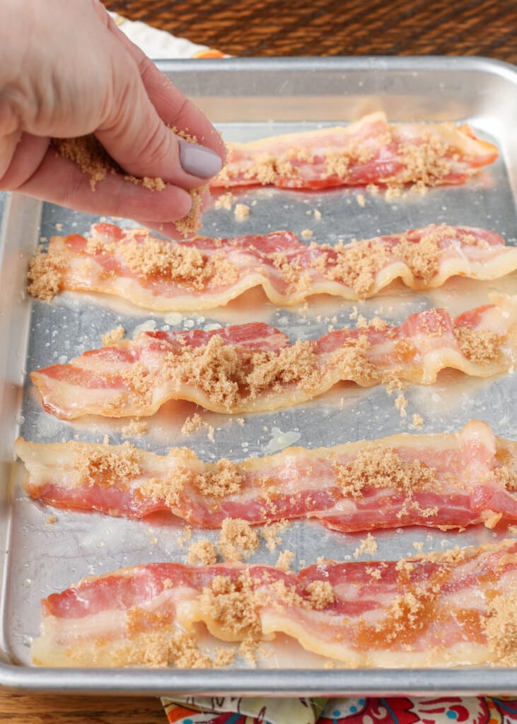 sprinkling brown sugar over bacon on sheet pan