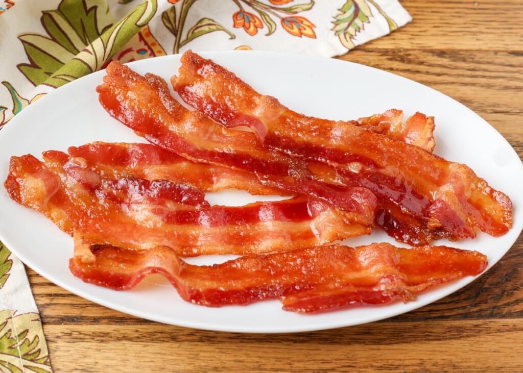 horizontal photo of shiny caramelized bacon on oval plate