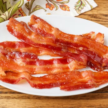 horizontal photo of shiny caramelized bacon on oval plate