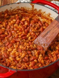 Baked beans with ground beef and bacon in red dutch oven with wooden spoon