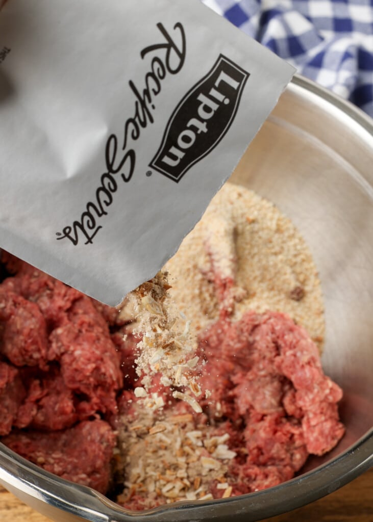 package of onion soup being added to meatloaf mixture in stainless bowl