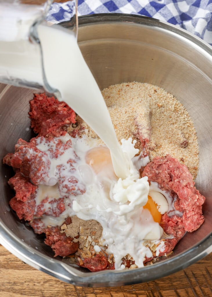 milk being added to meatloaf ingredients in metal bowl