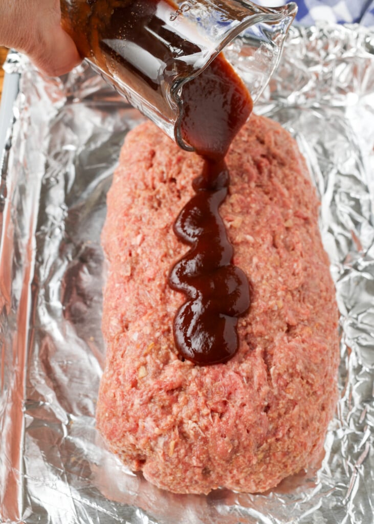glaze being poured over meatloaf on lined sheet pan