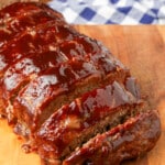 sliced meatloaf on board next to checkered blue napkin