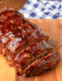 sliced meatloaf on board next to checkered blue napkin