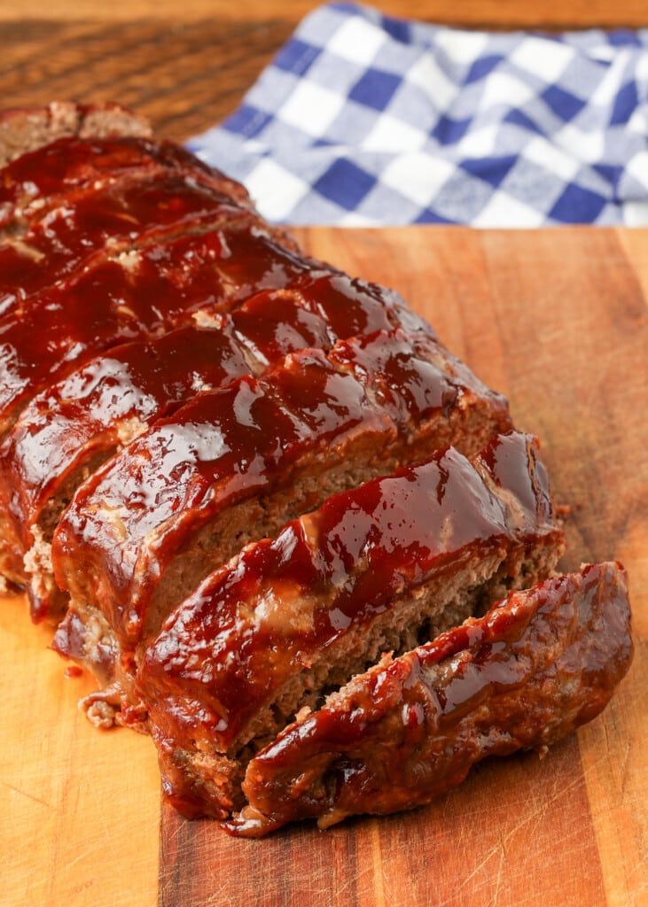 sliced meatloaf on board next to checkered blue napkin