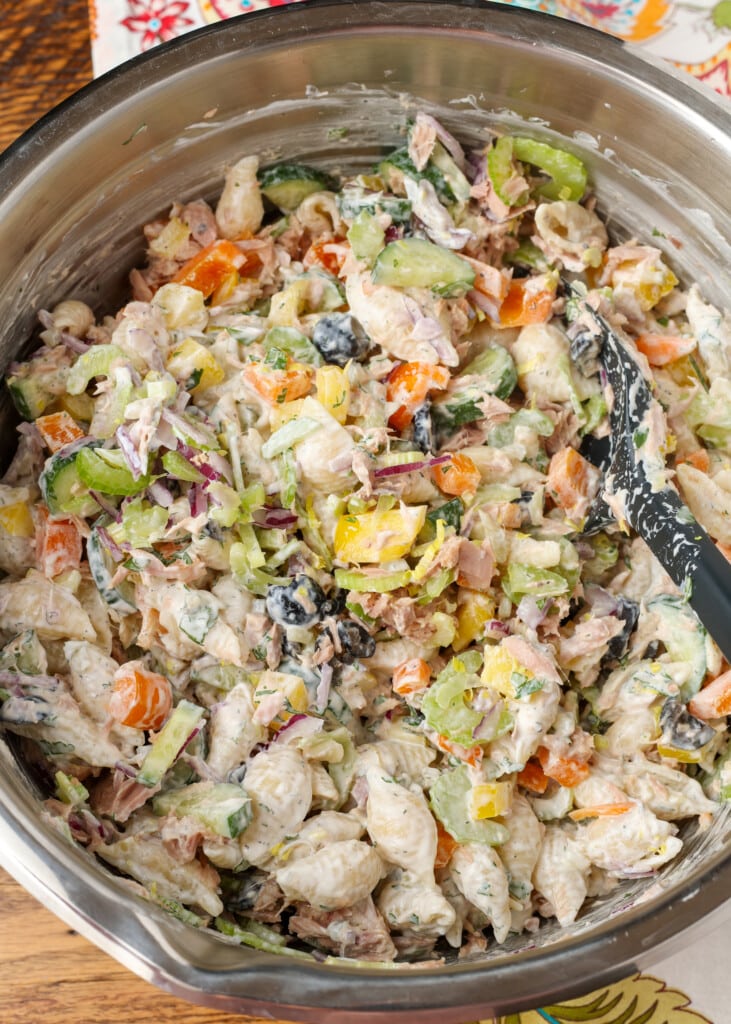 metal bowl holding pasta salad, black spatula stirring everything together