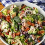 white bowl on wooden table holding broccoli salad with cranberries and bacon