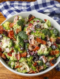 white bowl on wooden table holding broccoli salad with cranberries and bacon