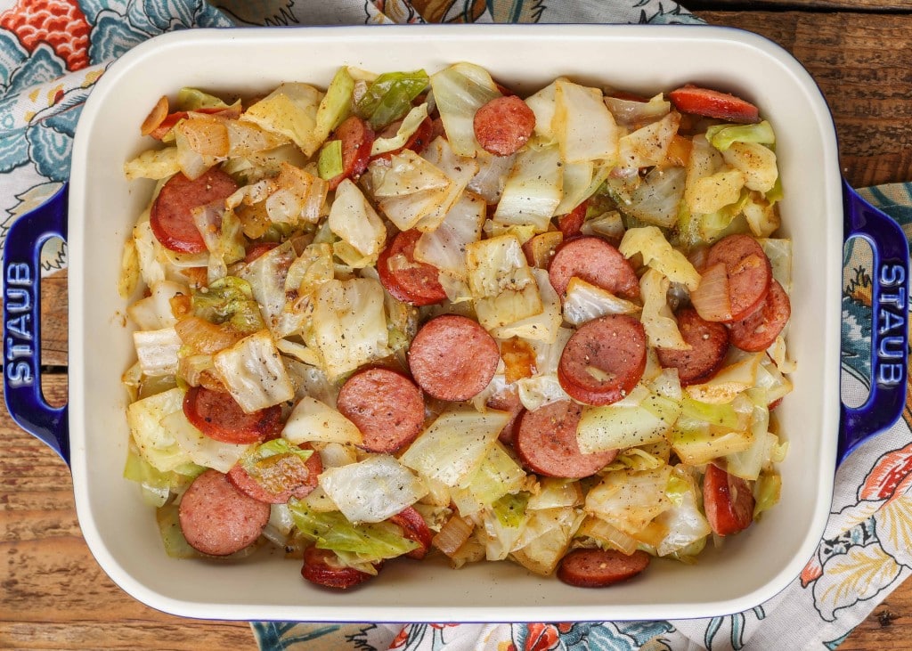 Overhead shot of kielbasa sausage and lettuce, served in a long white rectangular tray with black handles