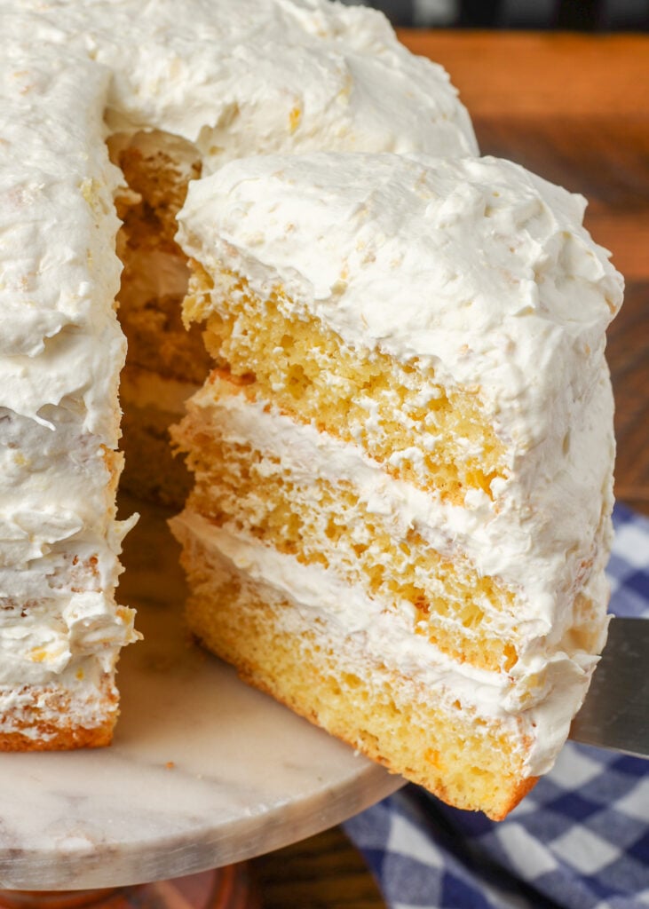 close up photo of frosted yellow cake with pineapple and oranges inside