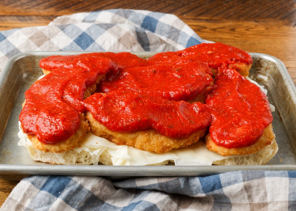 A horizontally aligned image showing the second layer of marinara over the chicken cutlets.