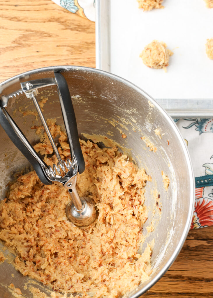 A cookie scoop rests atop the cookie down in a mixing bowl next to a baking sheet.