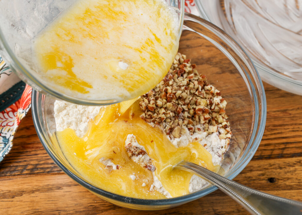 A vertically aligned action shot, showing the butter being poured over the other ingredients for the crust in a clear mixing bowl.