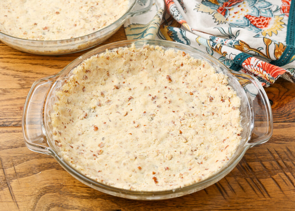 A vertically aligned image of a clear pie dish with the unbaked crust pressed into the bottom and sides, ready to go into the oven.