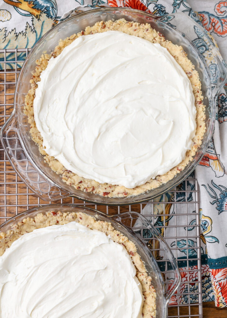 A vertically aligned image, showing that the bottom layer of cream cheese has been spread evenly over the bottom of each pie crust.