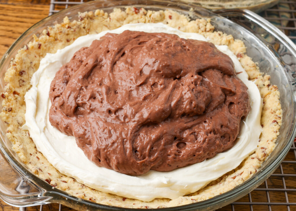 A horizontally aligned image showing the chocolate pudding that has been piled high over the cream cheese layer and is ready to be spread around.
