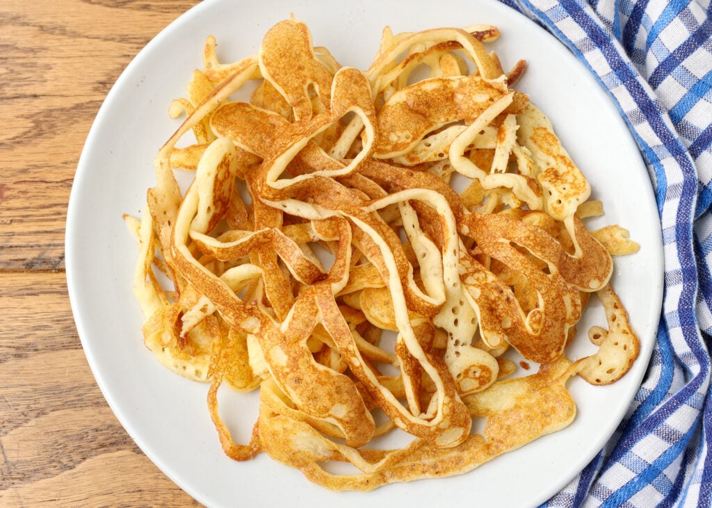 pancake spaghetti piled on white plate on wooden table