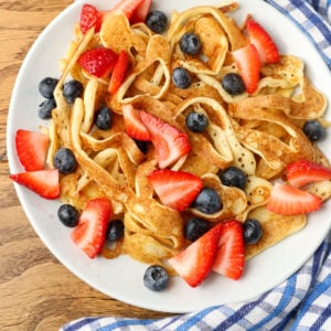 berries added to white plate holding pancake spaghetti