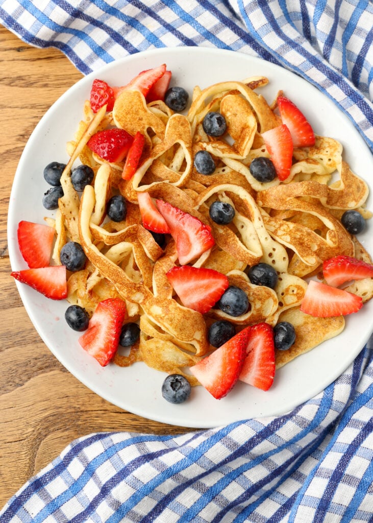berries added to white plate holding pancake spaghetti
